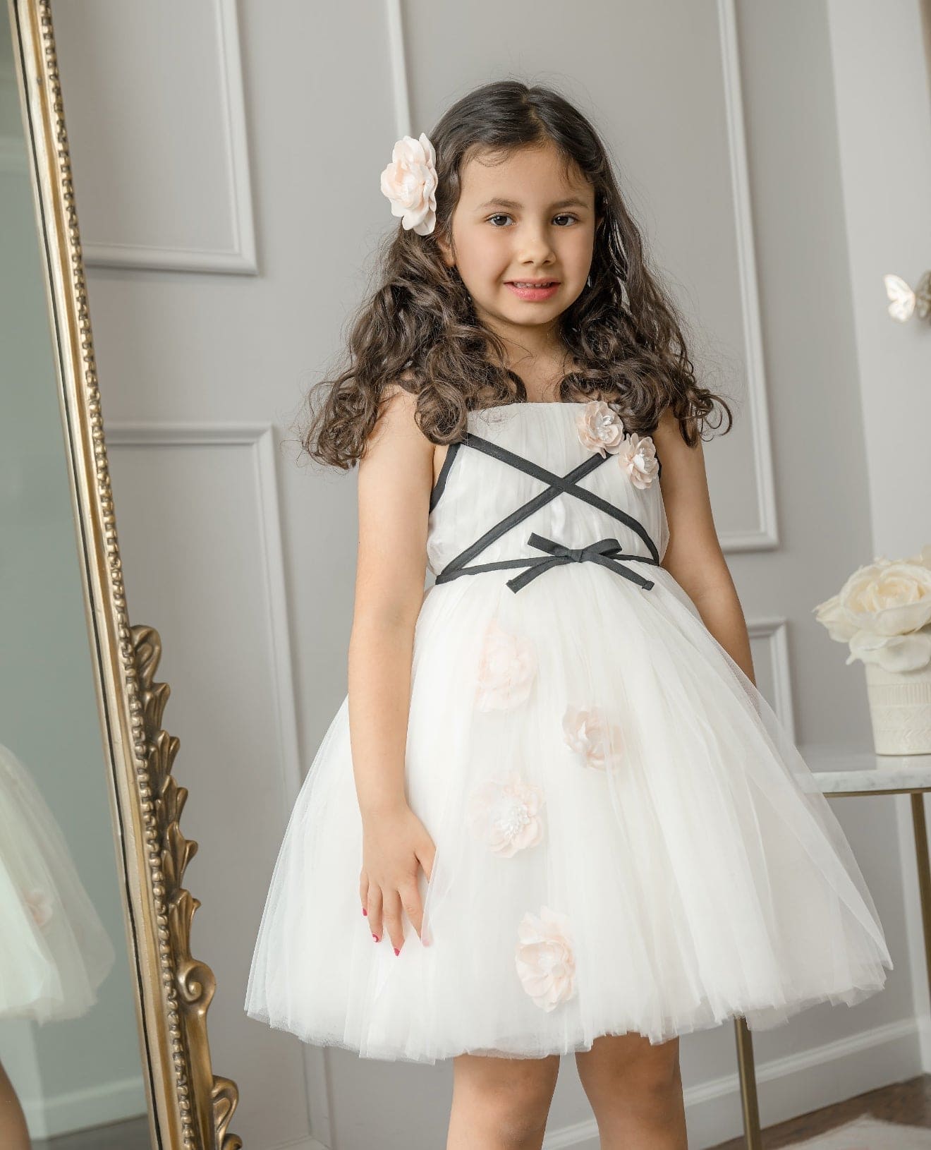 Giselle Ivory Criss-Cross dress that features tulle and flowers scattered along with black bow at the center of the dress.
