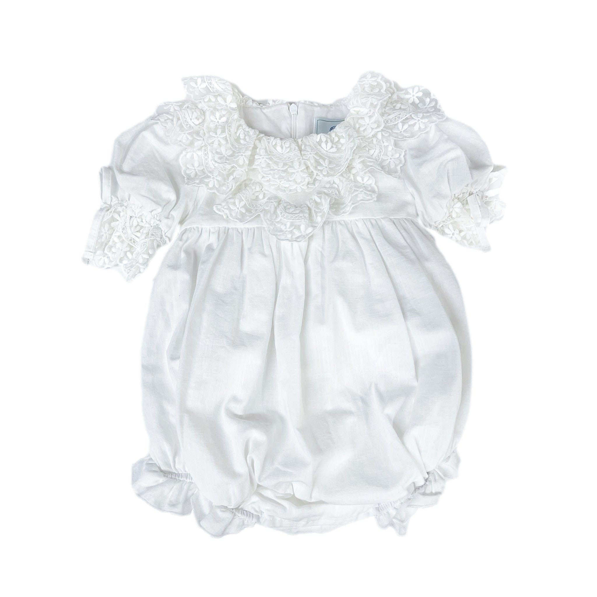 Katherine white linen baby girl romper with embroidered lace detail, large back tie bow, and zipper closure.