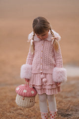 Young girl wearing pink cable cardigan with faux fur collar and cuffs, styled with skirt and satin hair bows