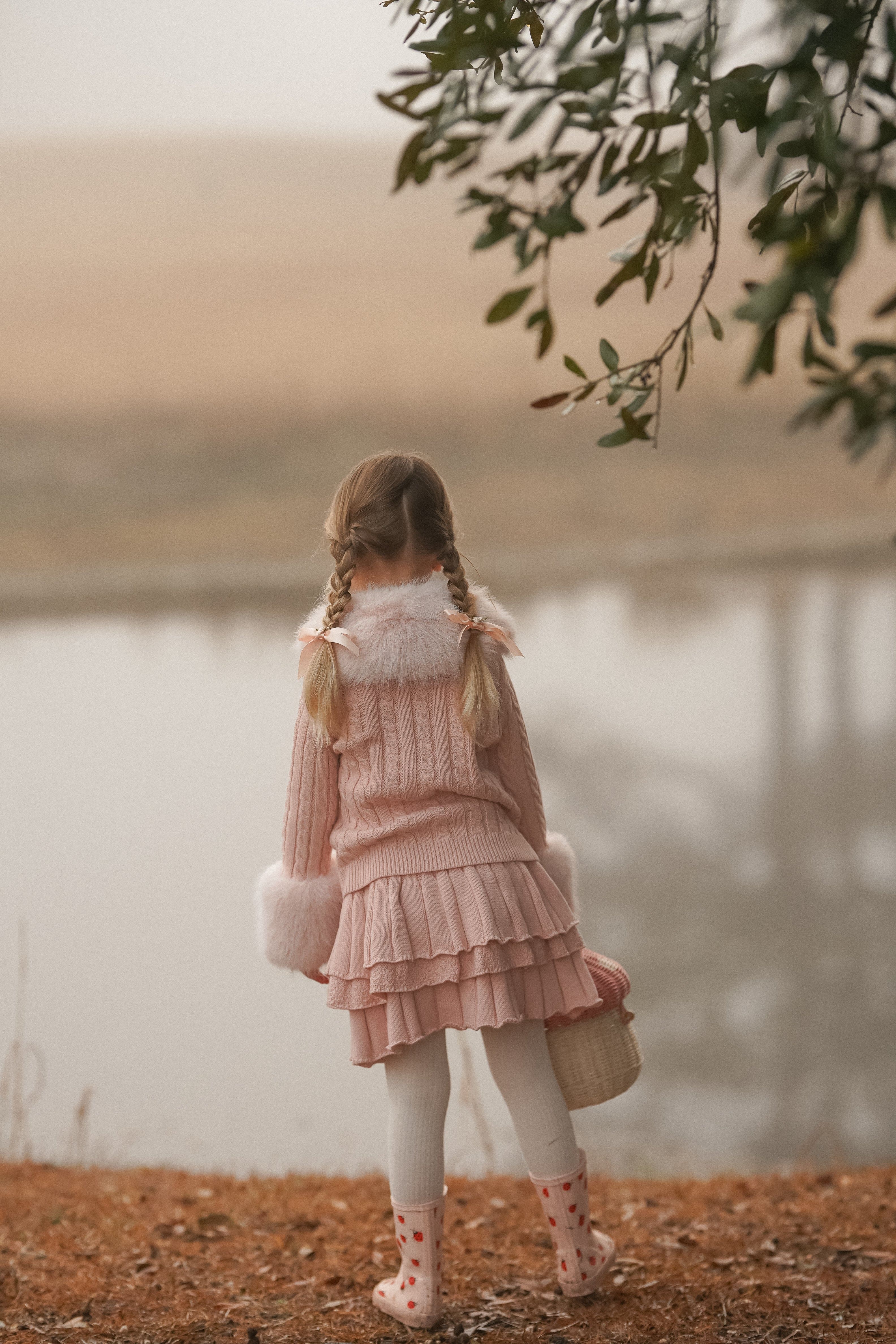 Back view of a child wearing a pink knit cardigan with faux fur collar and sleeve detail 