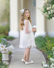 Young girl in a white dress standing outdoors with floral decorations.
