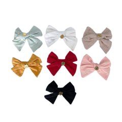 Linen hair bow with gold logo detail and secure back clasp, classic accessory available in multiple colors.
